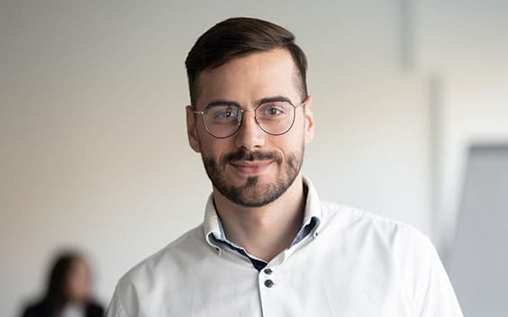 Young white man in an office, smiling.